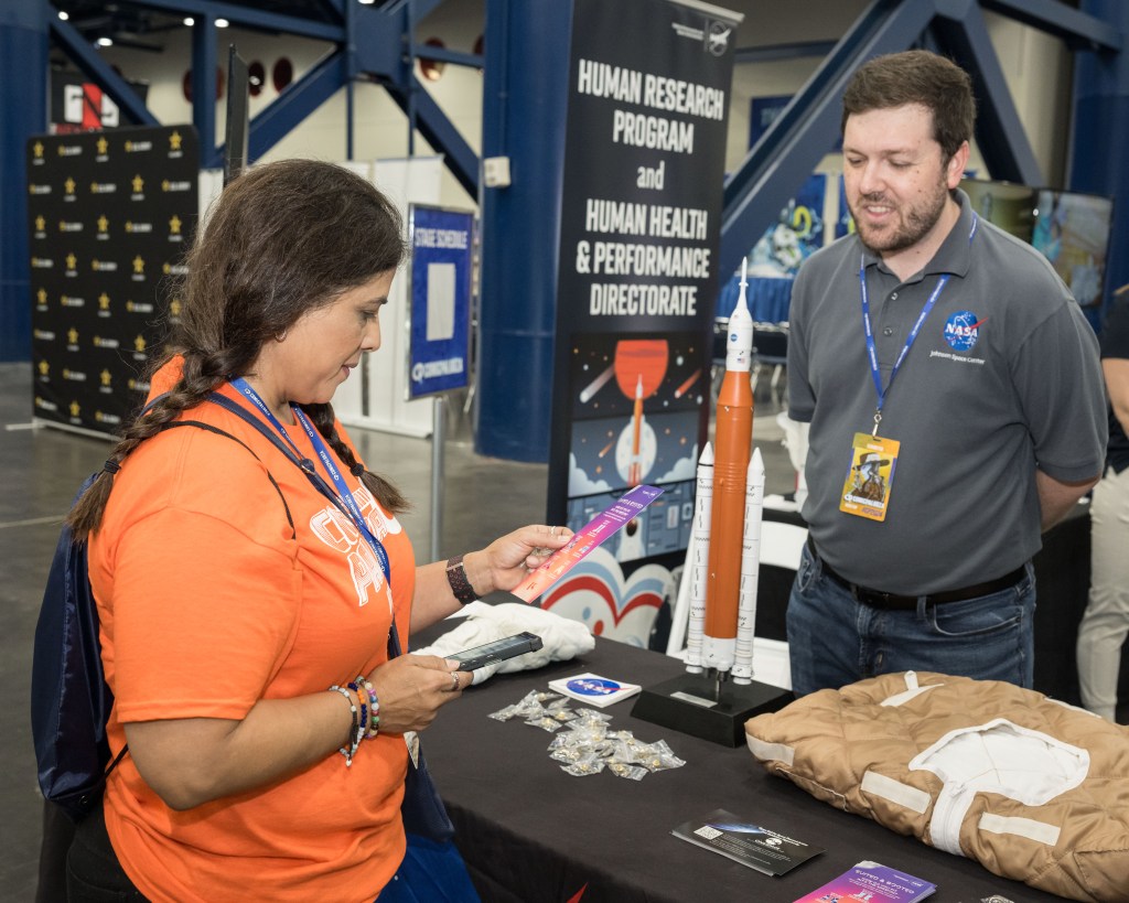 A woman visits a NASA table to learn about the Space Launch System.