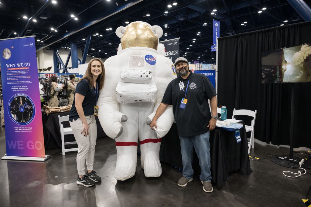 A man and a woman stand next to an inflatable astronaut mascot.