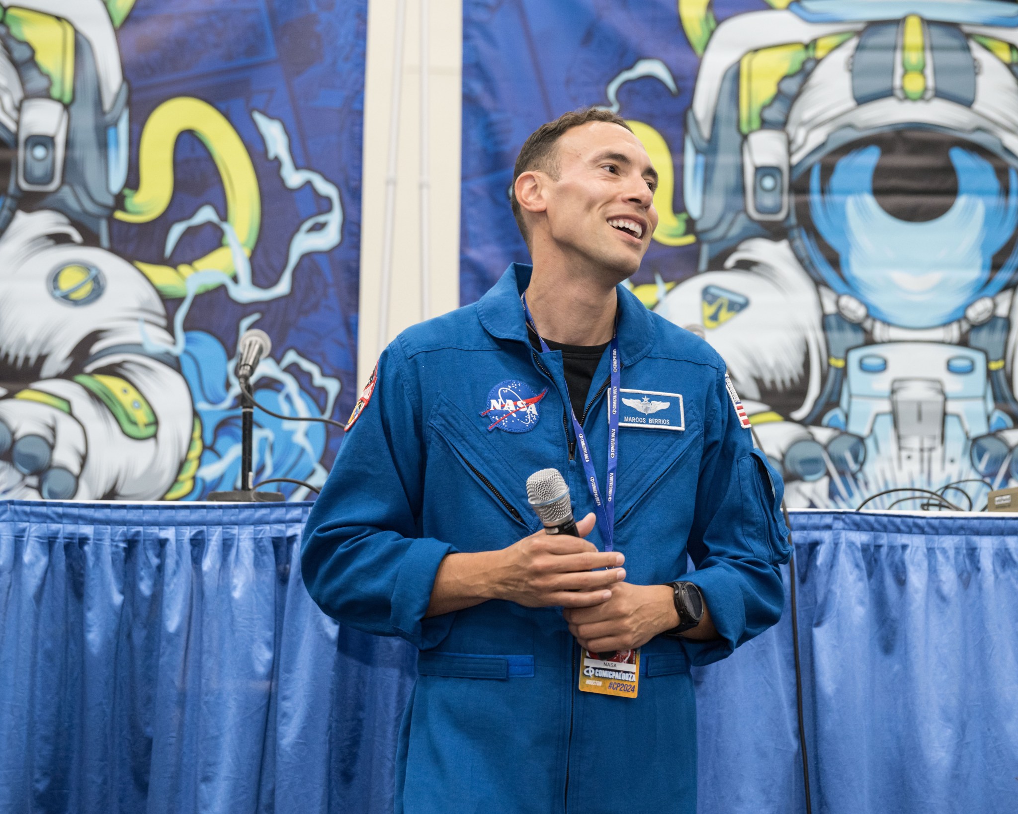 NASA astronaut Marcos Berrios holds a microphone while giving a presentation at Comicpalooza.