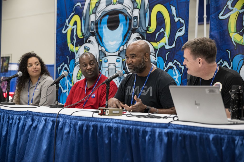 A diverse group of children and adults enjoy a NASA exhibit booth at Comicpalooza.