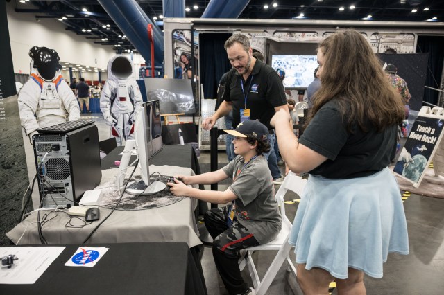 A diverse group of children and adults enjoy a NASA exhibit booth at Comicpalooza.