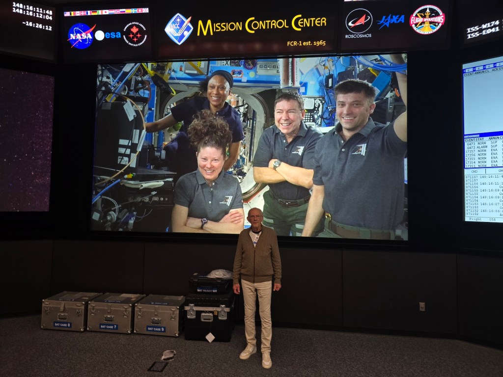 Actor Christopher Lloyd stands in front of a large screen at Johnson Space Center's Mission Control Center.