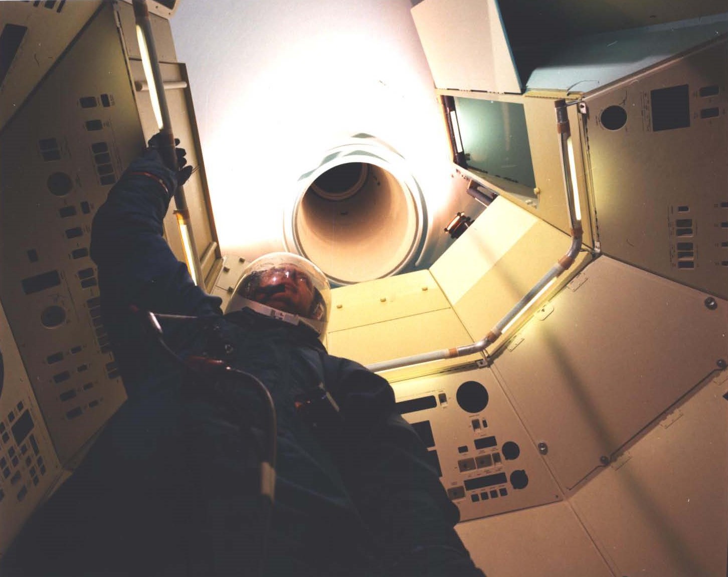 Medium fidelity mockup of the MOL crew cabin, with suited crew member and the narrow tunnel leading to the Gemini-B capsule