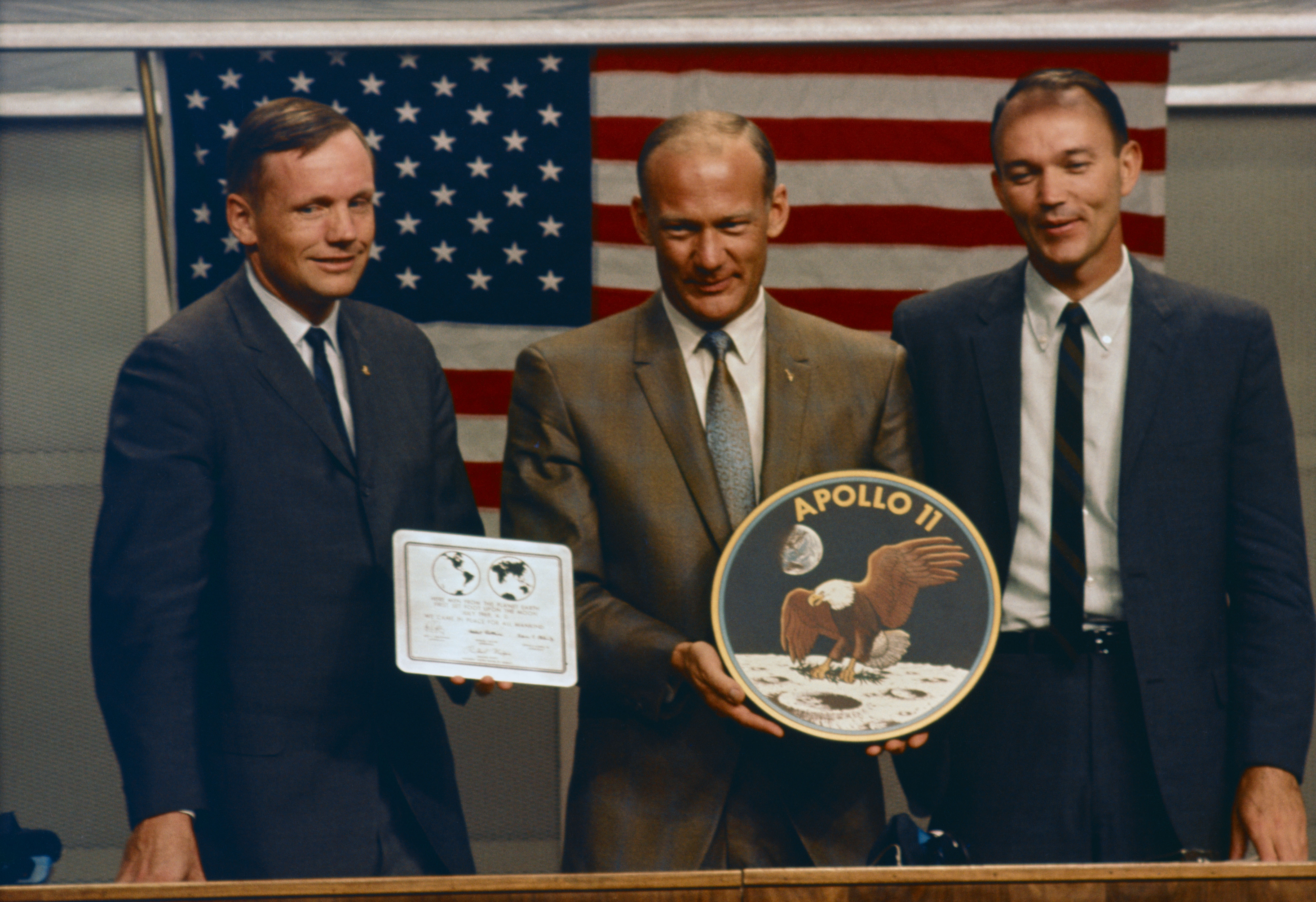 Apollo 11 astronauts Neil A. Armstrong, left, Edwin E. “Buzz” Aldrin, and Michael Collins hold a copy of the commemorative plaque they will leave behind on the Moon and their mission patch