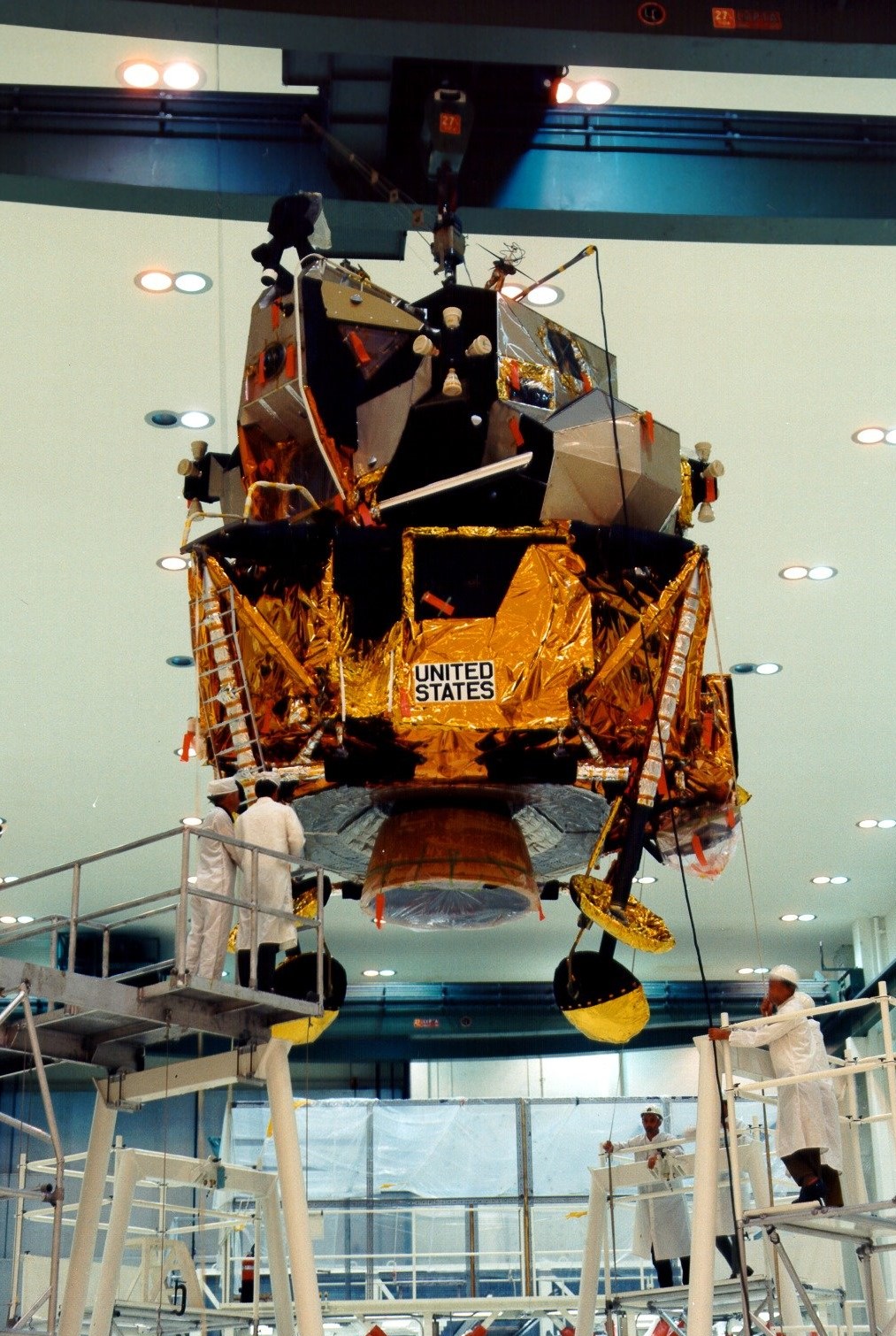 In the Manned Spacecraft Operations Building (MSOB) at NASA's Kennedy Space Center, workers finish attaching the landing gear to the Apollo 12 Lunar Module (LM)