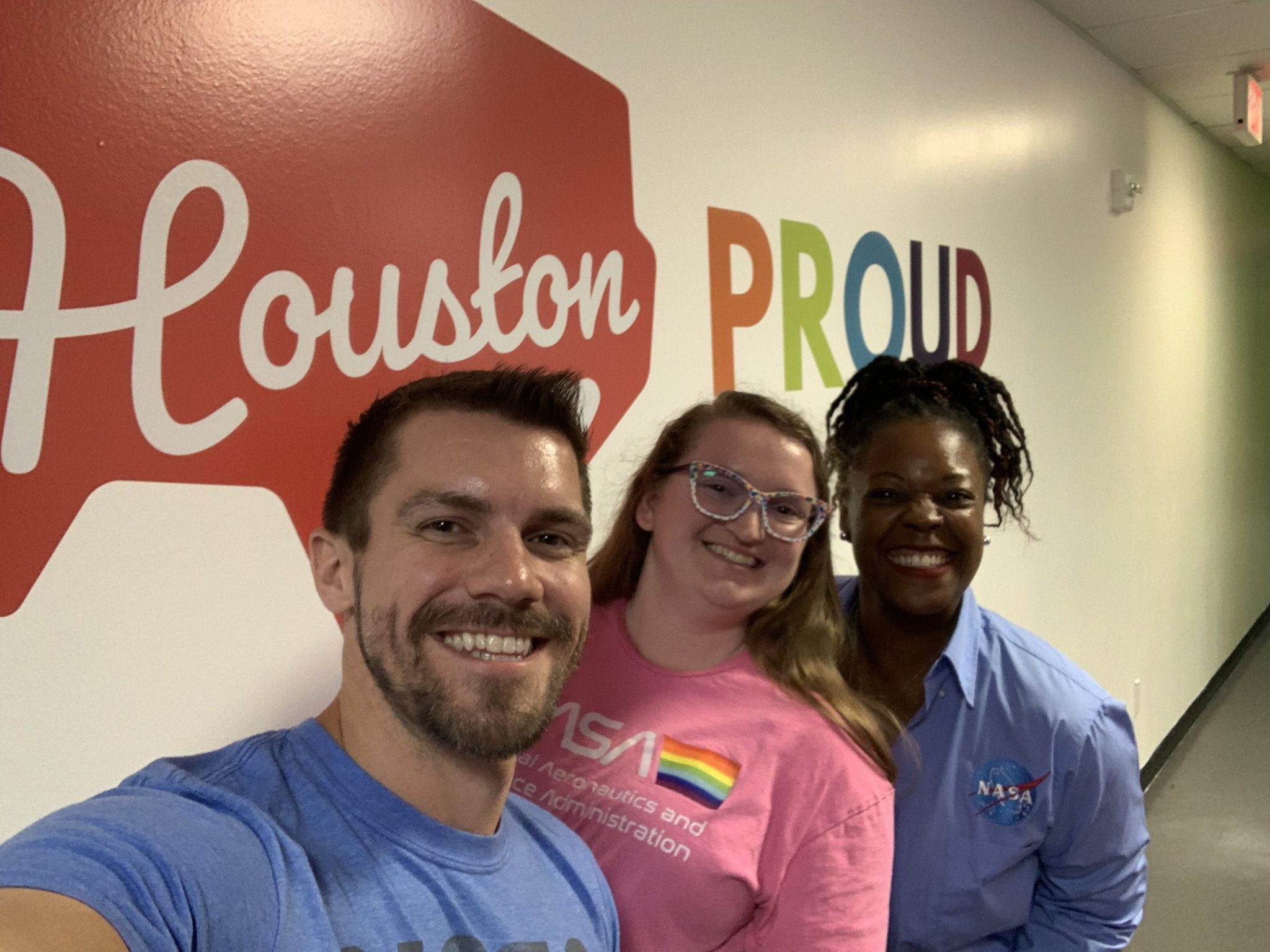 A white man, white woman, and black woman wear NASA shirts while volunteering for a Montrose Center LGBTQI+ event in Houston.