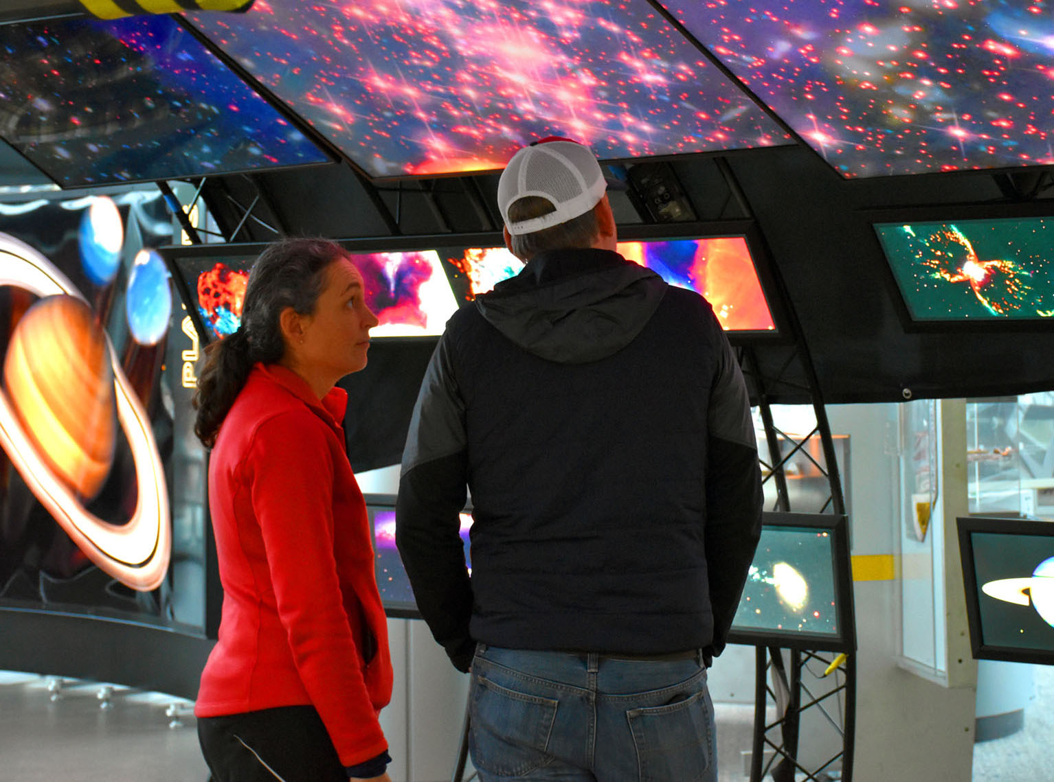 Two visitors stand under an arch of Hubble Space Telescope images and admire views of the cosmos. 