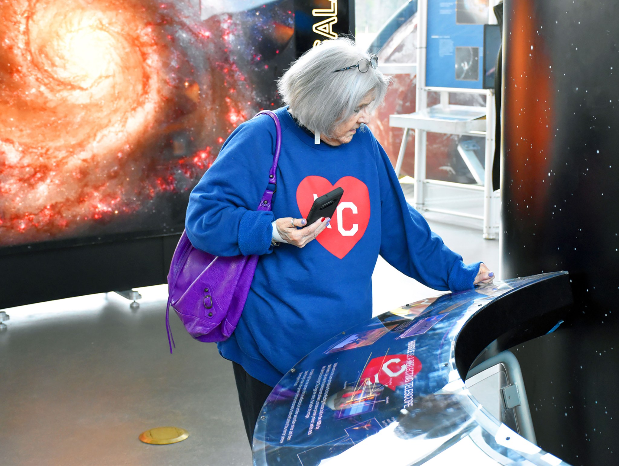 A guest stands in front of a kiosk in the Hubble Space Telescope travelling exhibit. A large image of a spiral galaxy is backlit behind her.