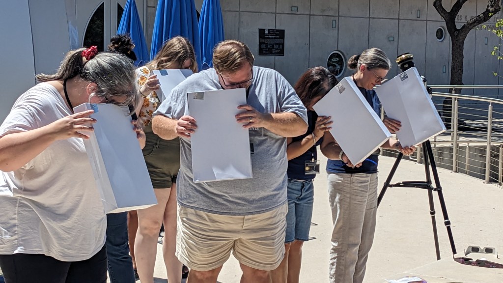 A group of people testing out their “cereal box” pin-hole viewers to study the sun