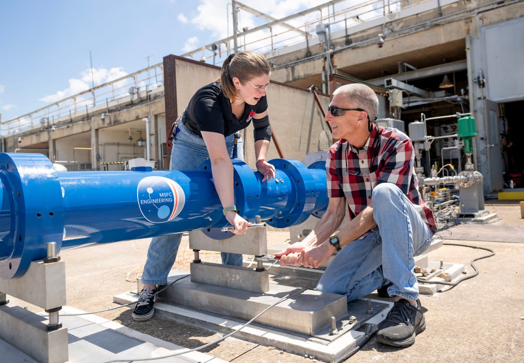 A pair of NASA engineers conduct checkout testing of a new hybrid rocket engine testbed, a long, blue, cylindrical facility for testing new government and industry rocket motor hardware, materials, and propellants at NASA’s Marshall Space Flight Center.