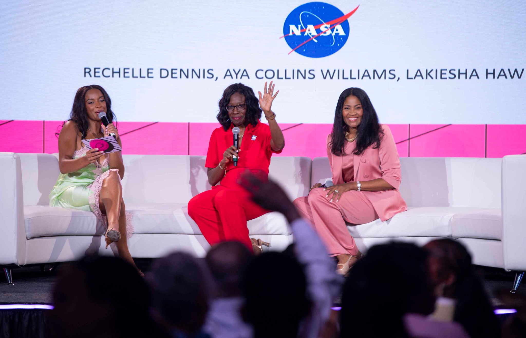 A 3-member panelists of women sit on a white sofa to lead Taking Up Space conversation at Essence Fest; The NASA meatball can be seen on the screen in the background