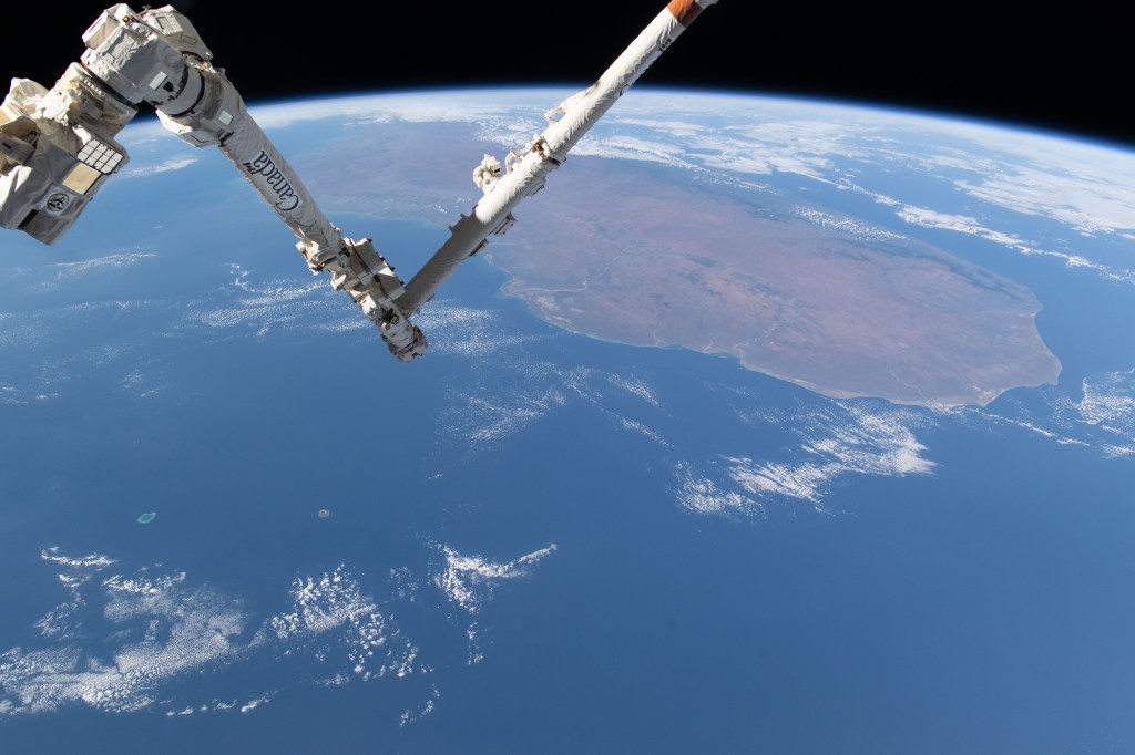 The International Space Station's 57.7-foot-long Canadarm2 robotic arm crosses the foreground as the orbital outpost soared 265 miles above the Mozambique Channel south of the African island nation of Madagascar.