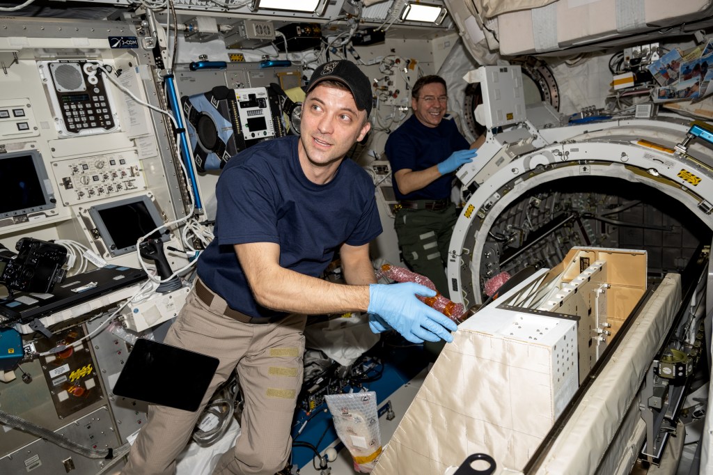 (From left) NASA astronauts Matthew Dominick and Mike Barratt, both Expedition 71 Flight Engineers, install the NanoRacks external platform inside the Kibo laboratory module's airlock. The platform from NanoRacks can host a variety of payloads placed outside the International Space Station and exposed to the external space environment for science experiments, technology demonstrations, and more.