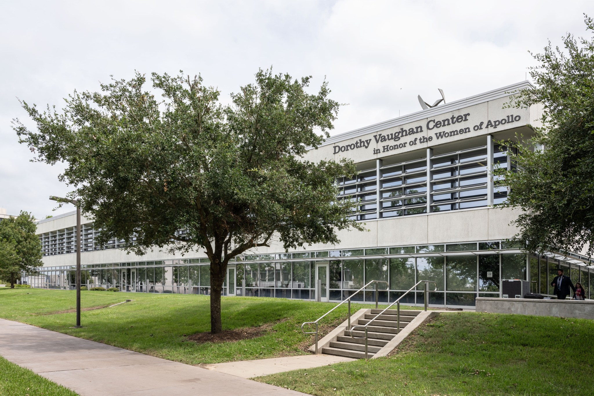 The image shows the exterior of a building named “Dorothy Vaughan Center in Honor of the Women of Apollo.” The building features modern architecture with large windows and a flat roof.