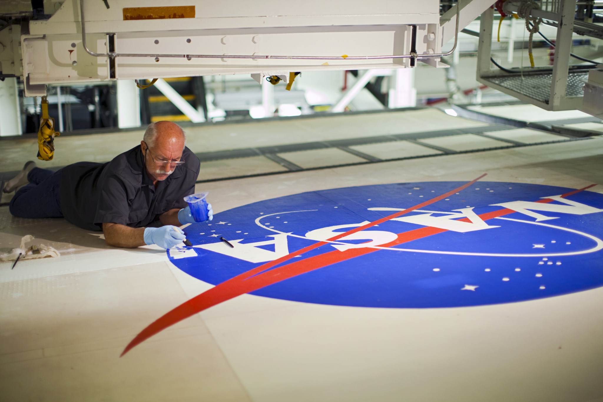 Image of a man on the ground painting blue on the NASA meatball logo.