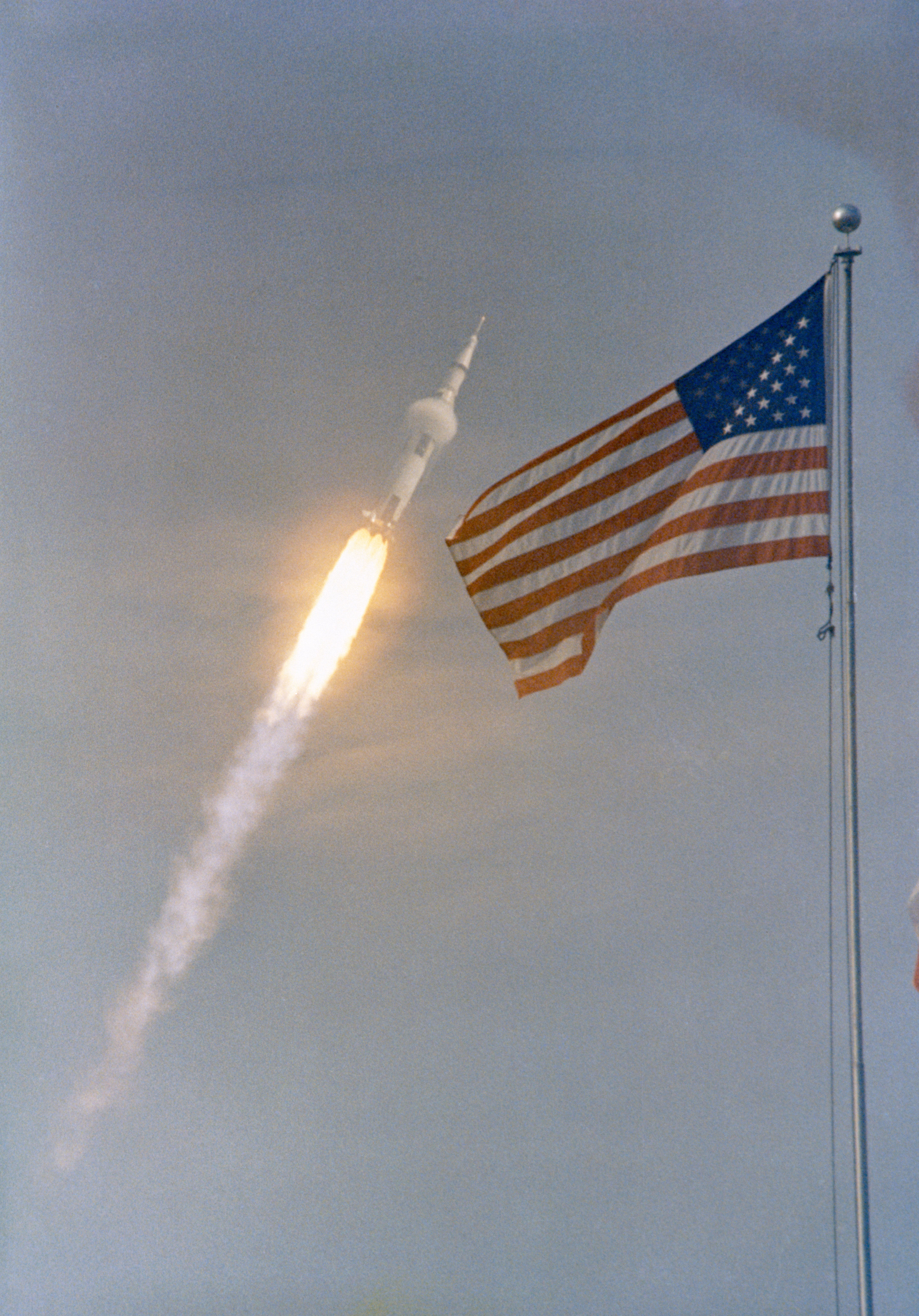 The American flag is pictured in the foreground as the Saturn V rocket for the historic Apollo 11 mission soars through the sky