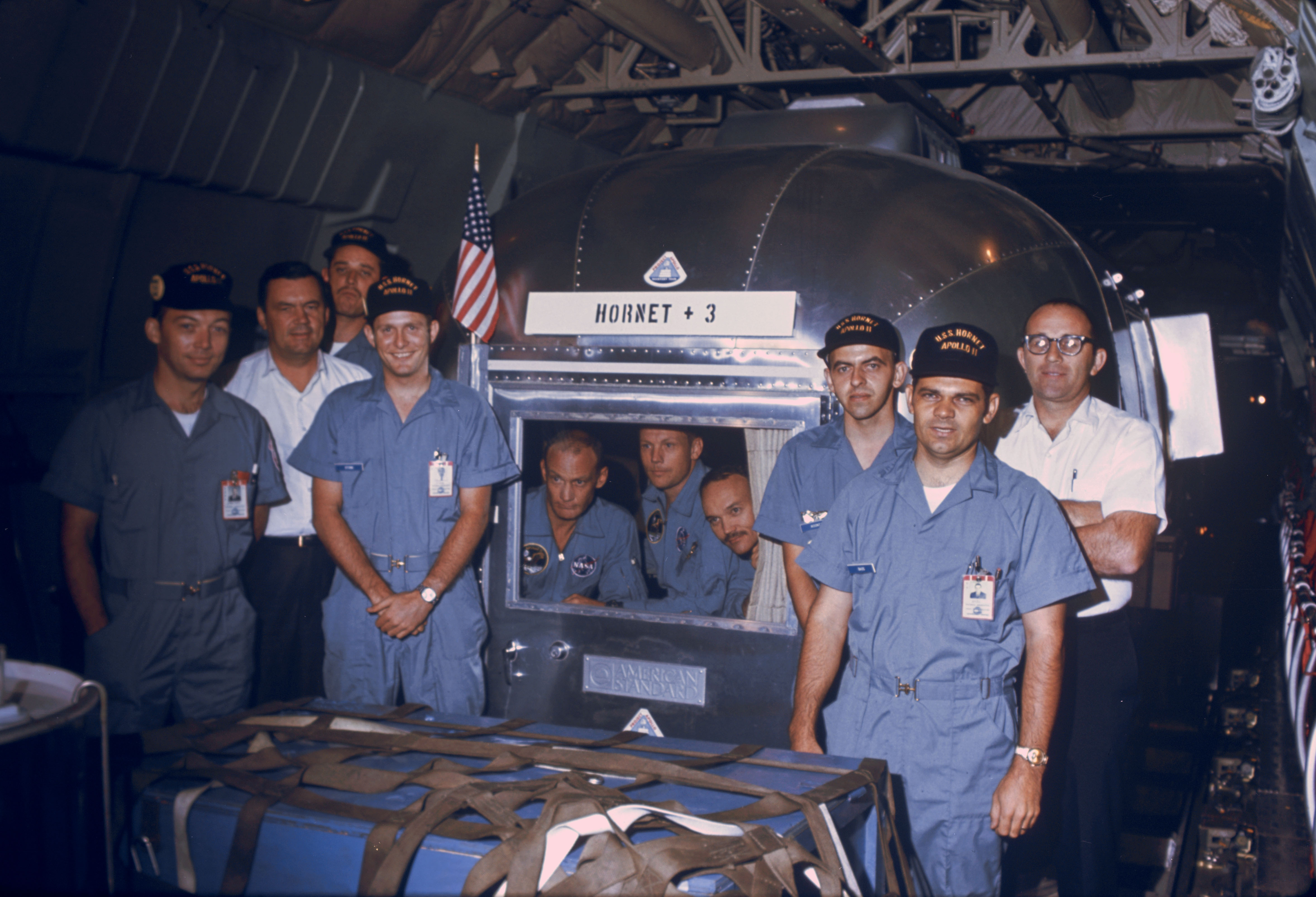 During the eight-hour flight, NASA recovery team members pose with Neil, Mike, and Buzz, seen through the window of the MQF