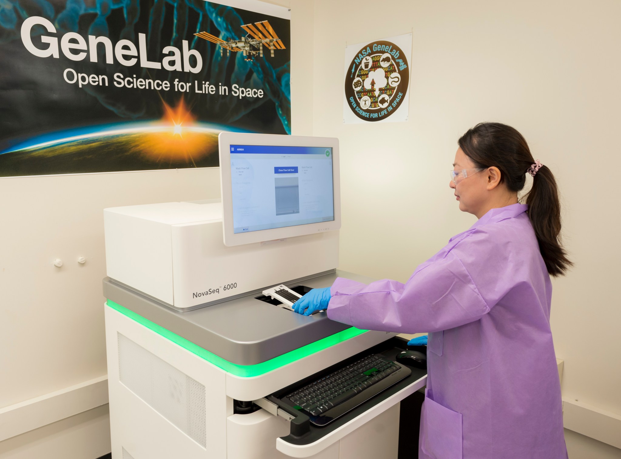 A woman at the sample processing machine with a GeneLab poster abover her