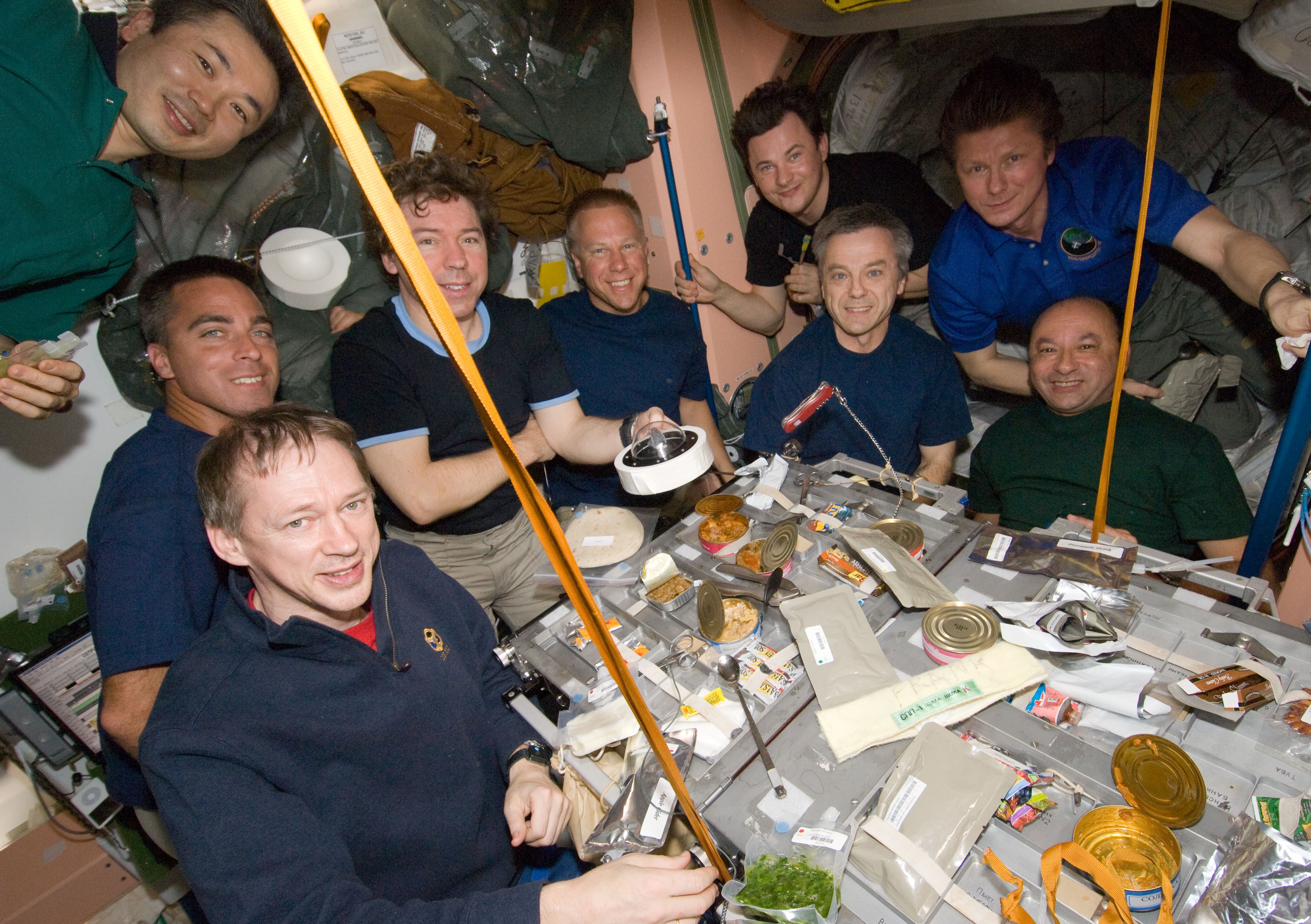 Nine of the 13 Expedition 20 and STS-127 crew members share a meal, as NASA astronaut Michael R. Barratt holds the Apollo 11 Moon rock