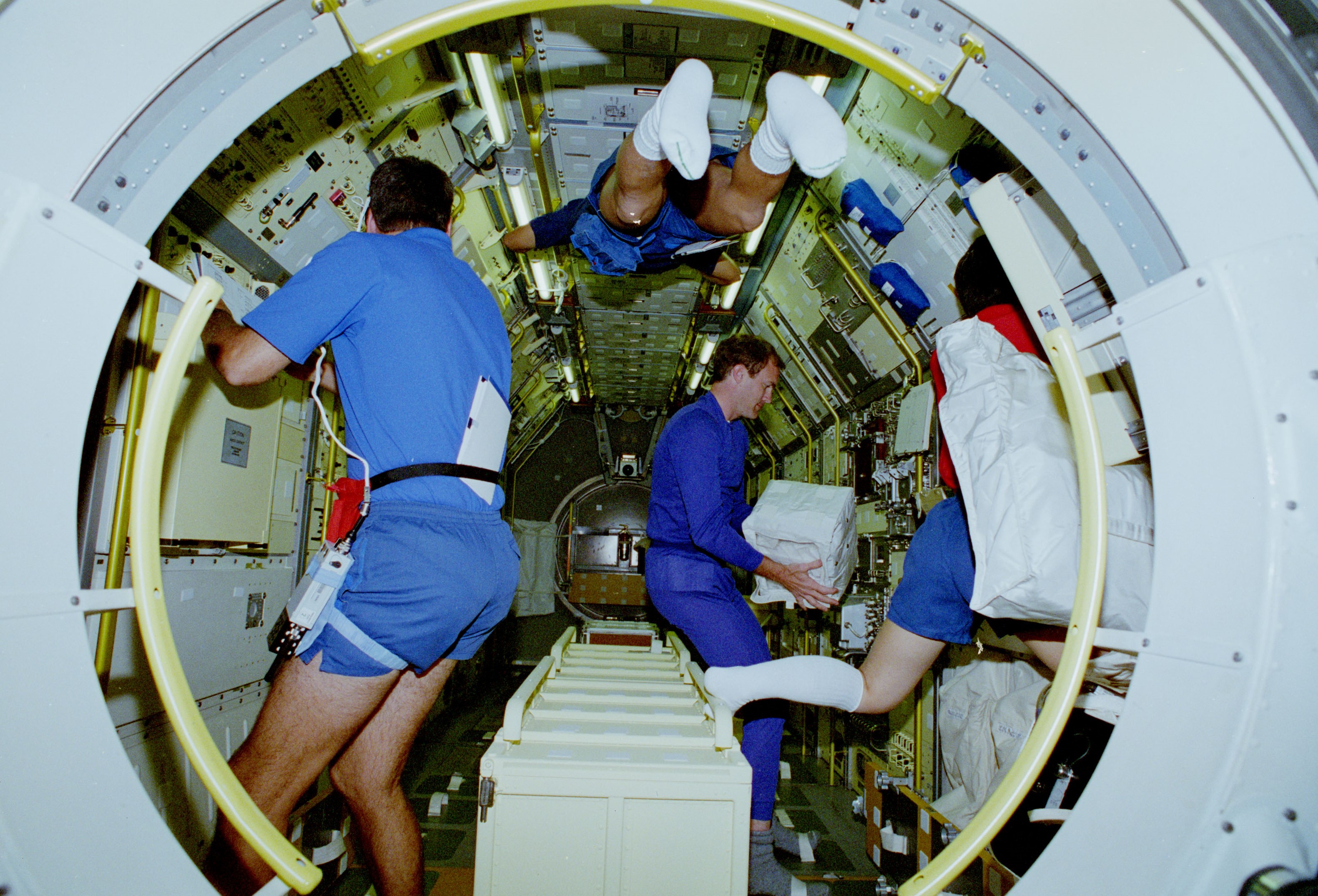 The view from the tunnel showing astronauts at work in the Spacelab module