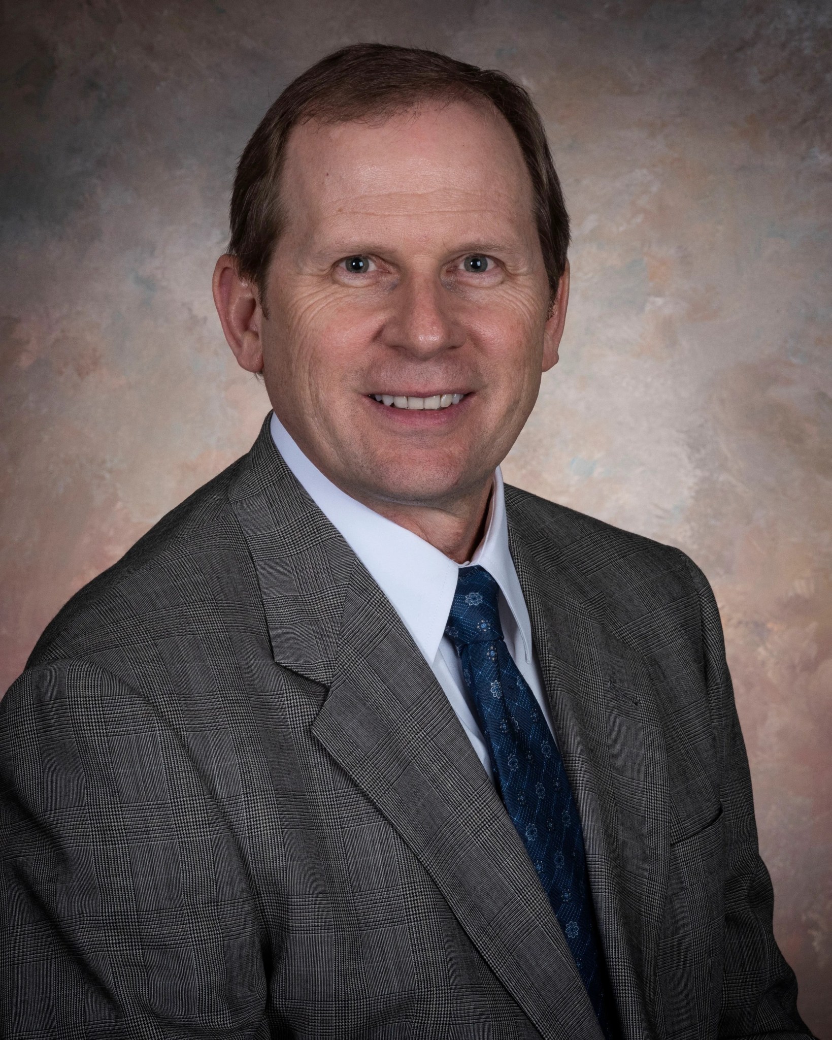 A headshot of an older white male in a grey suit