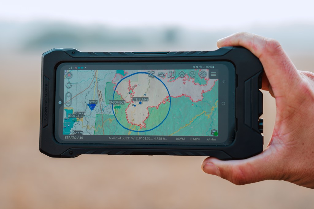 Improving Firefighter Safety with STRATO - A hand holding a small rectangular screen showing a map with an area circled.