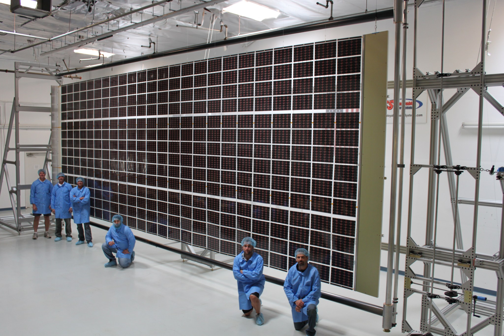 Six members in blue lab suits stand in front of a power grid.