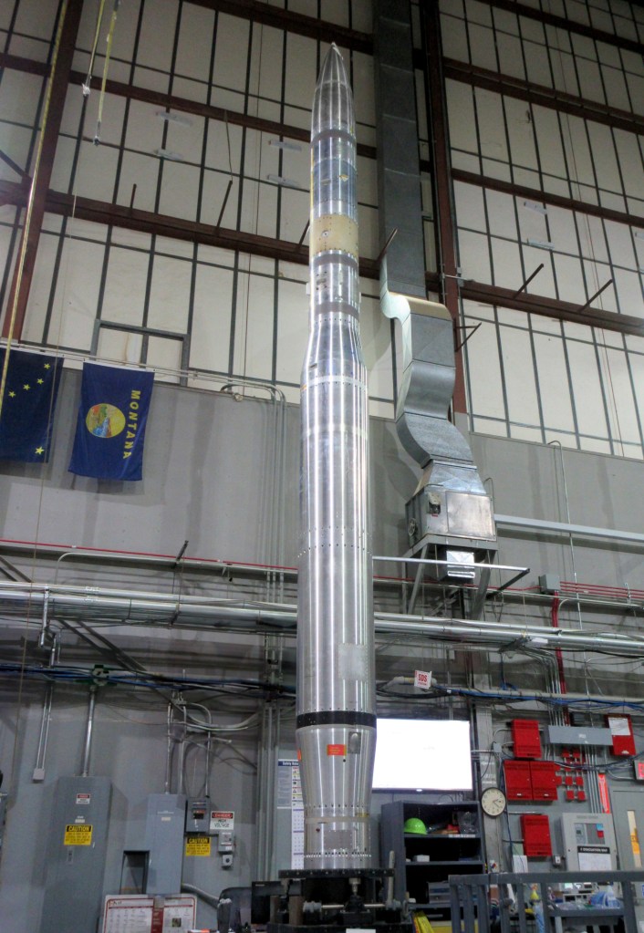 A silver sounding rocket stands in a room for testing.