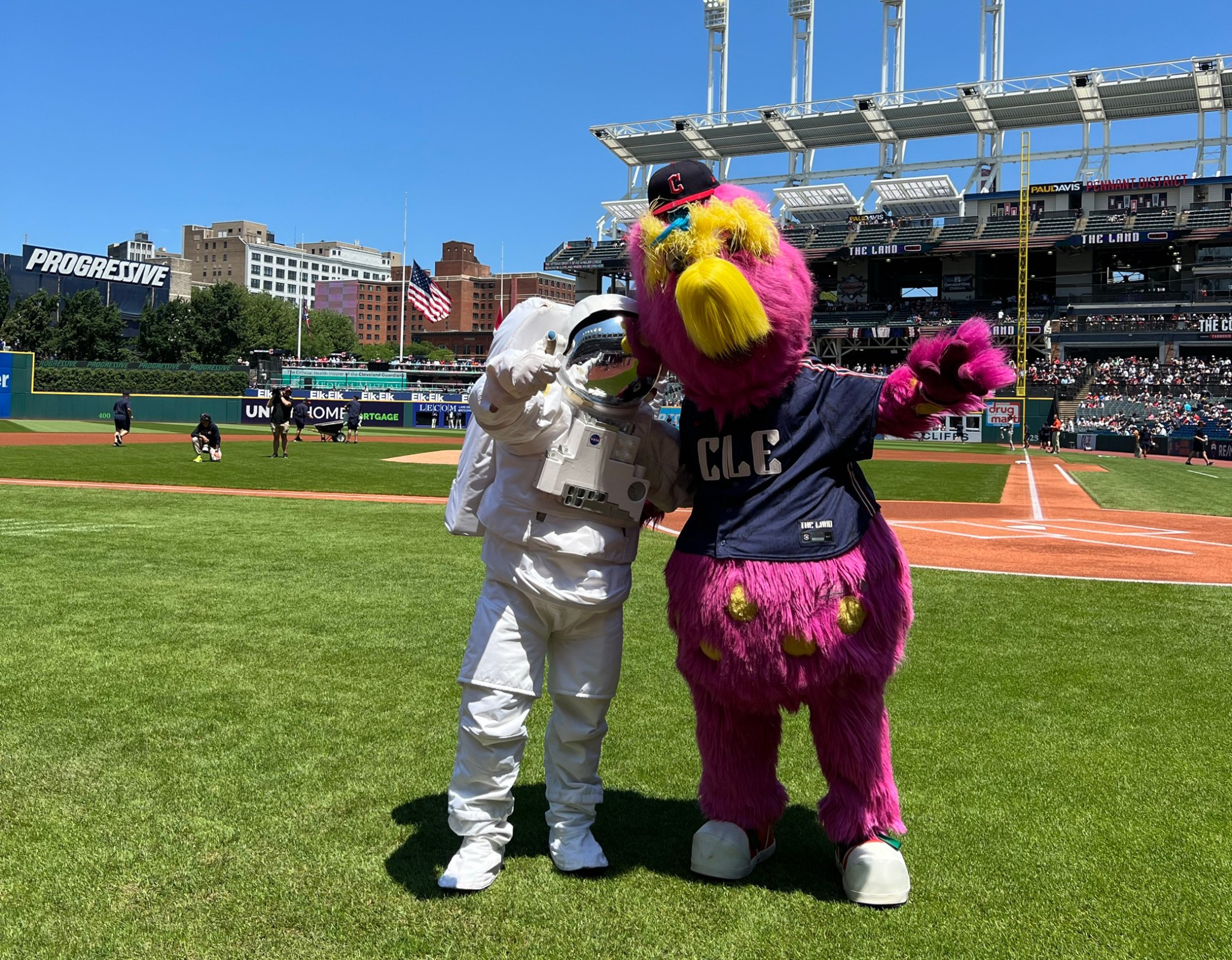 An astronaut mascot and Guardians mascot pose next to each other on the baseball field.