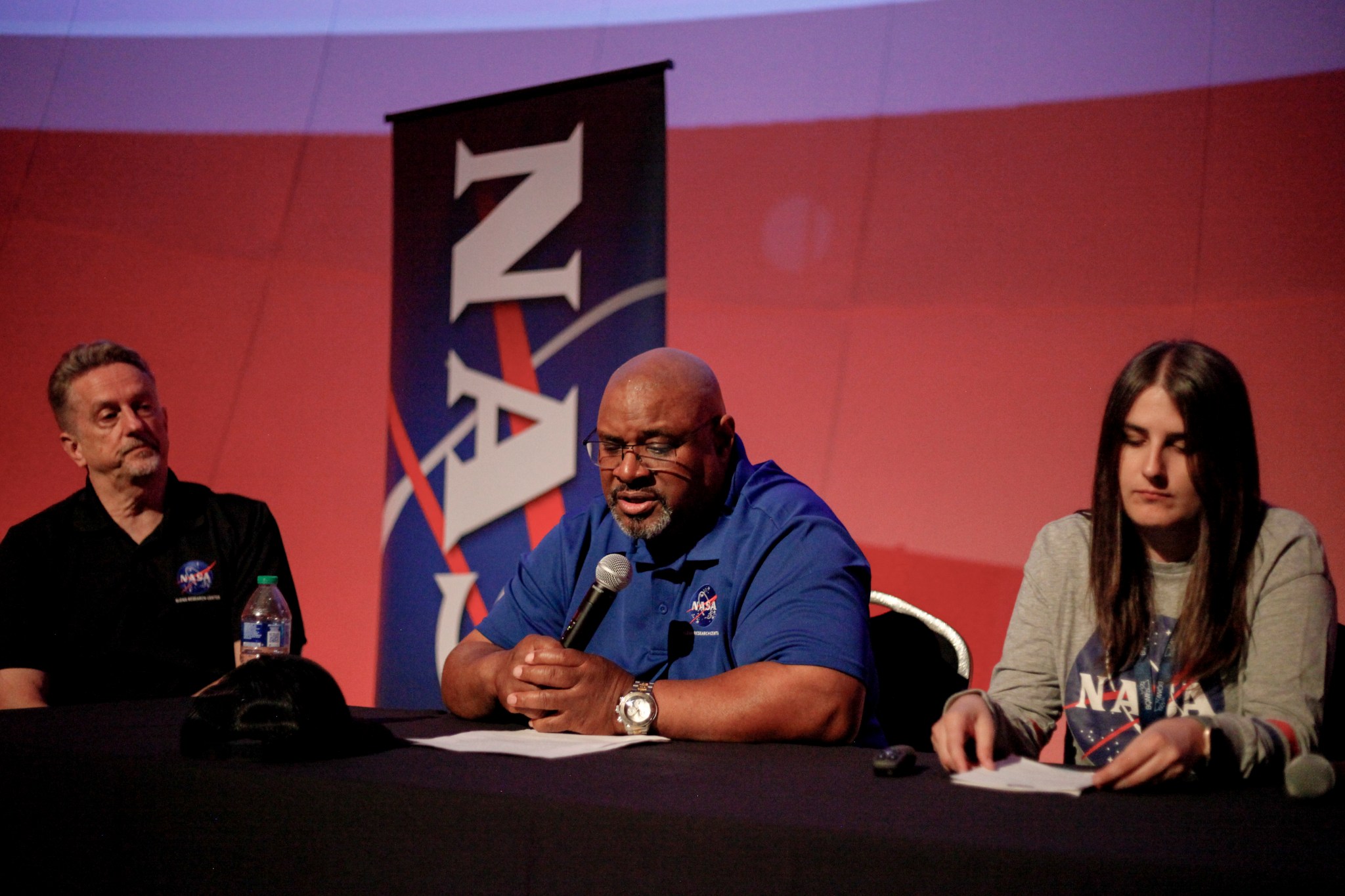 Three people sit at table with a NASA banner in the back.