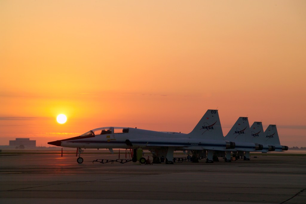 A line of NASA T-38 jets parked on a runway during sunrise.