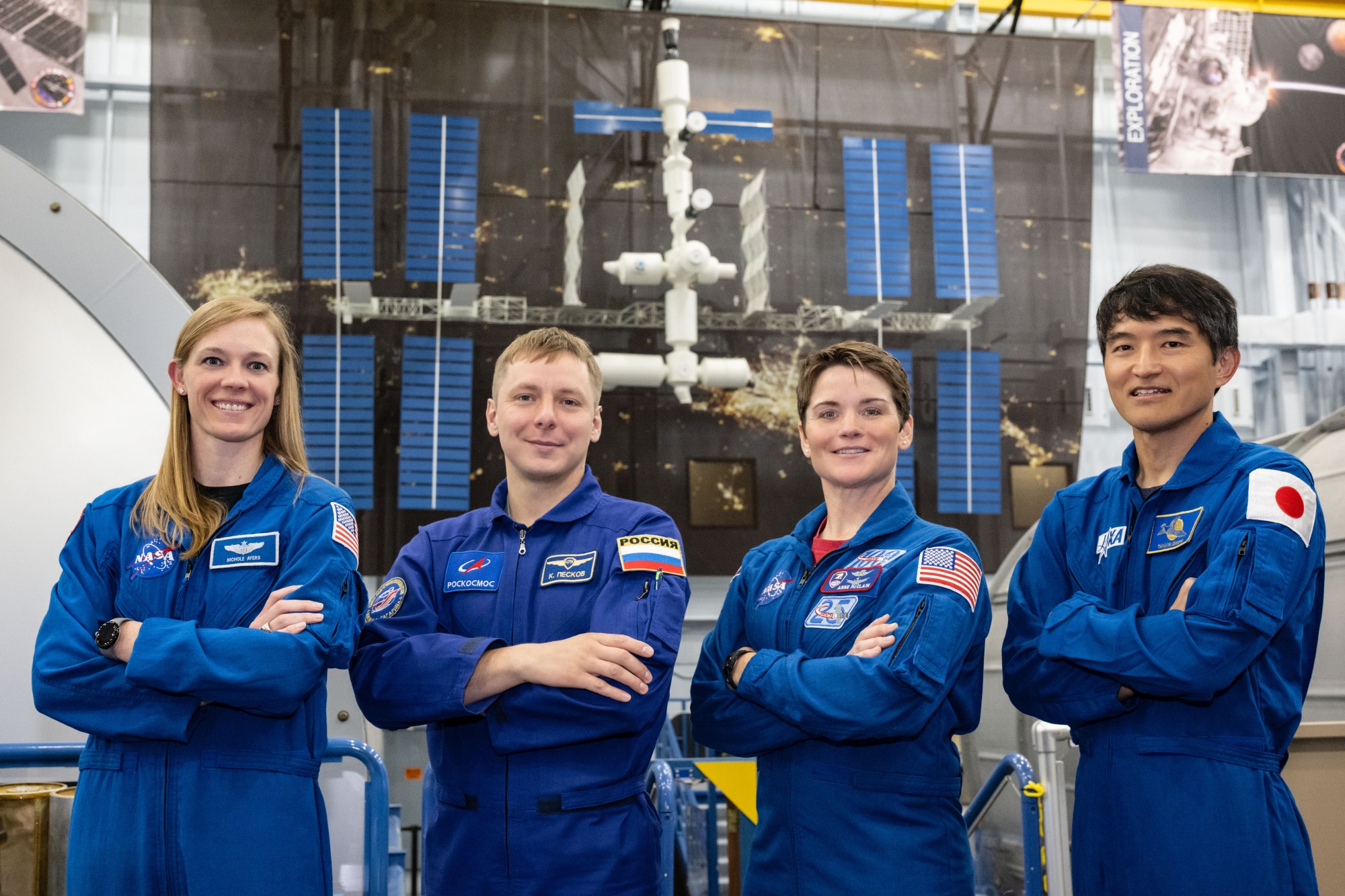 Photo of four NASA SpaceX Crew-10 flight crew members in blue flight suits with their arms crossed and smiling.