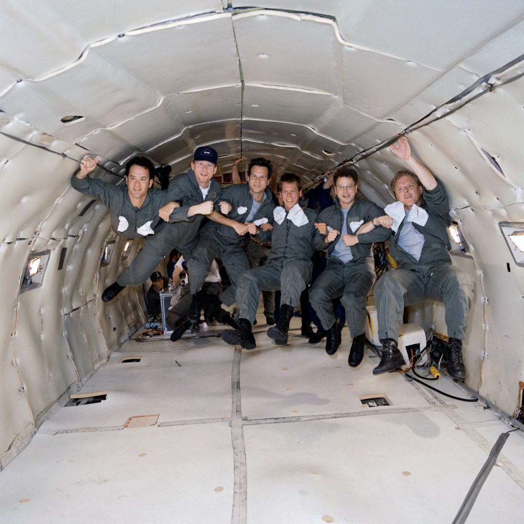 A group of six people inside an aircraft cabin designed for parabolic flight. The group is floating in mid-air, demonstrating weightlessness.