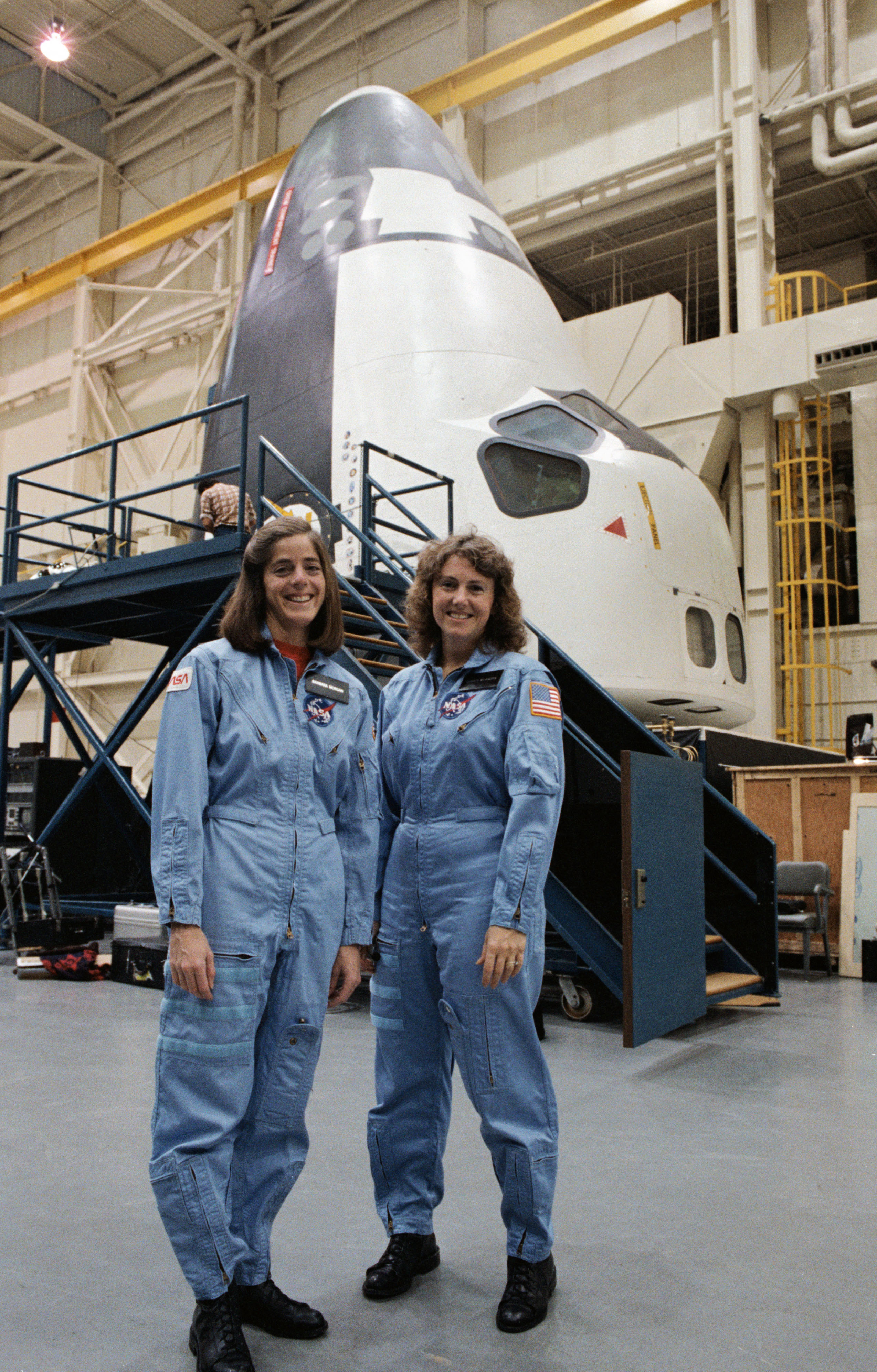 Barbara R. Morgan and S. Christa McAuliffe pose in front of the space shuttle crew compartment trainer