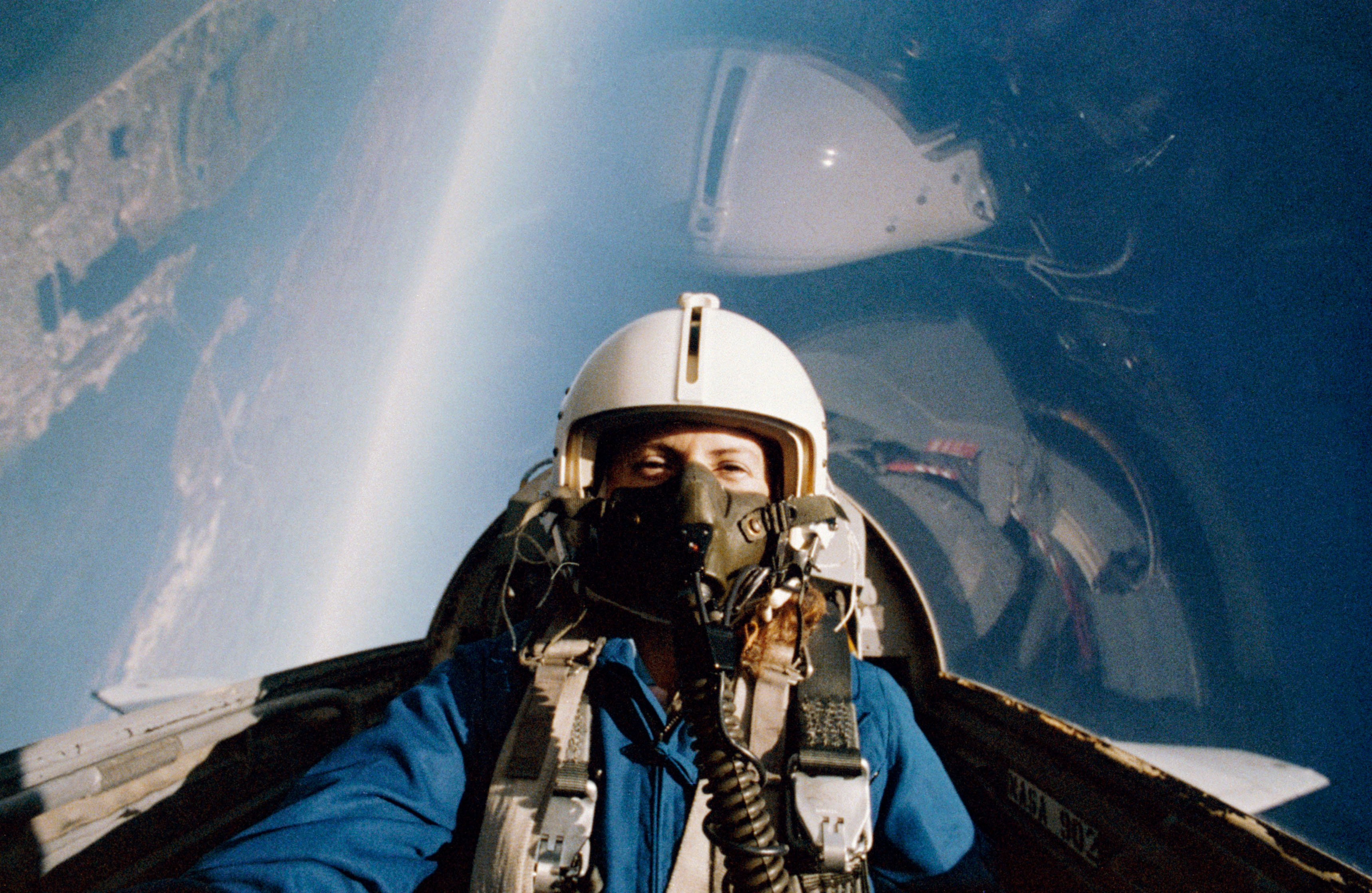 Teacher in Space designee S. Christa McAuliffe in the backseat of a T-38 jet trainer during a right turn, with part of Galveston Island visible at left