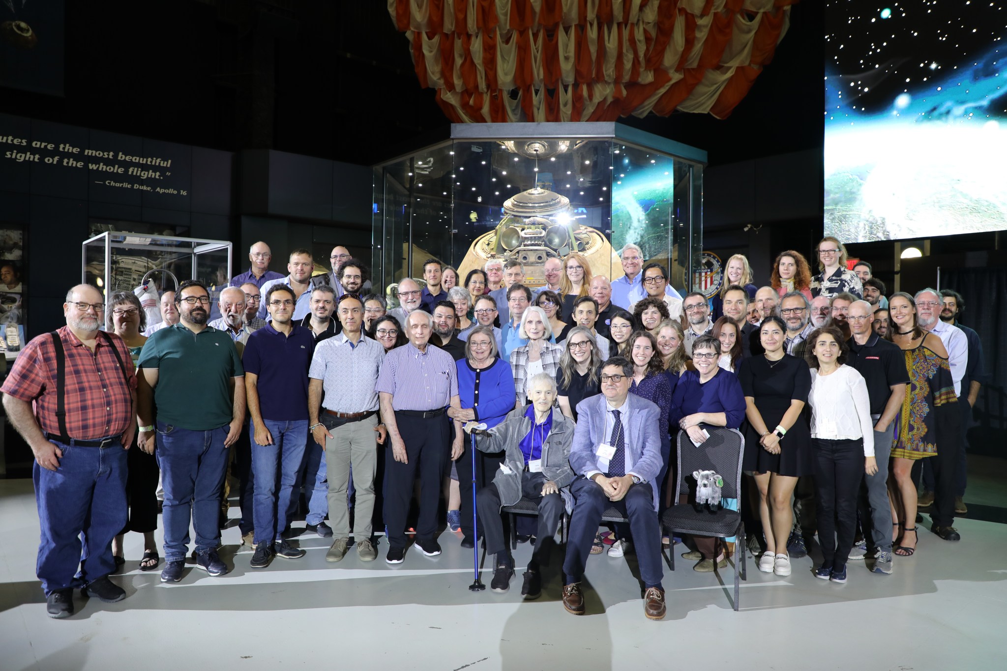 Rossi Prize winners Weisskopf and Soffitta, center seated, are joined by a plush goat, the unofficial mascot of the IXPE mission, and other IXPE team members at the Rossi Prize Recognition Dinner.