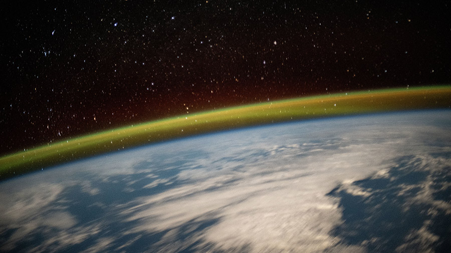 Stars glitter above a yellow-green atmospheric glow crowning Earth's horizon nn this long-duration shot taken by NASA astronaut Jeanette Epps.