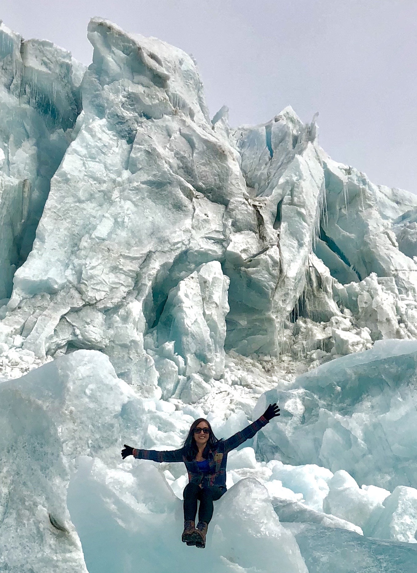 Linette Boisvert sits on a large light blue glacier with her arms stretched out to both sides. 