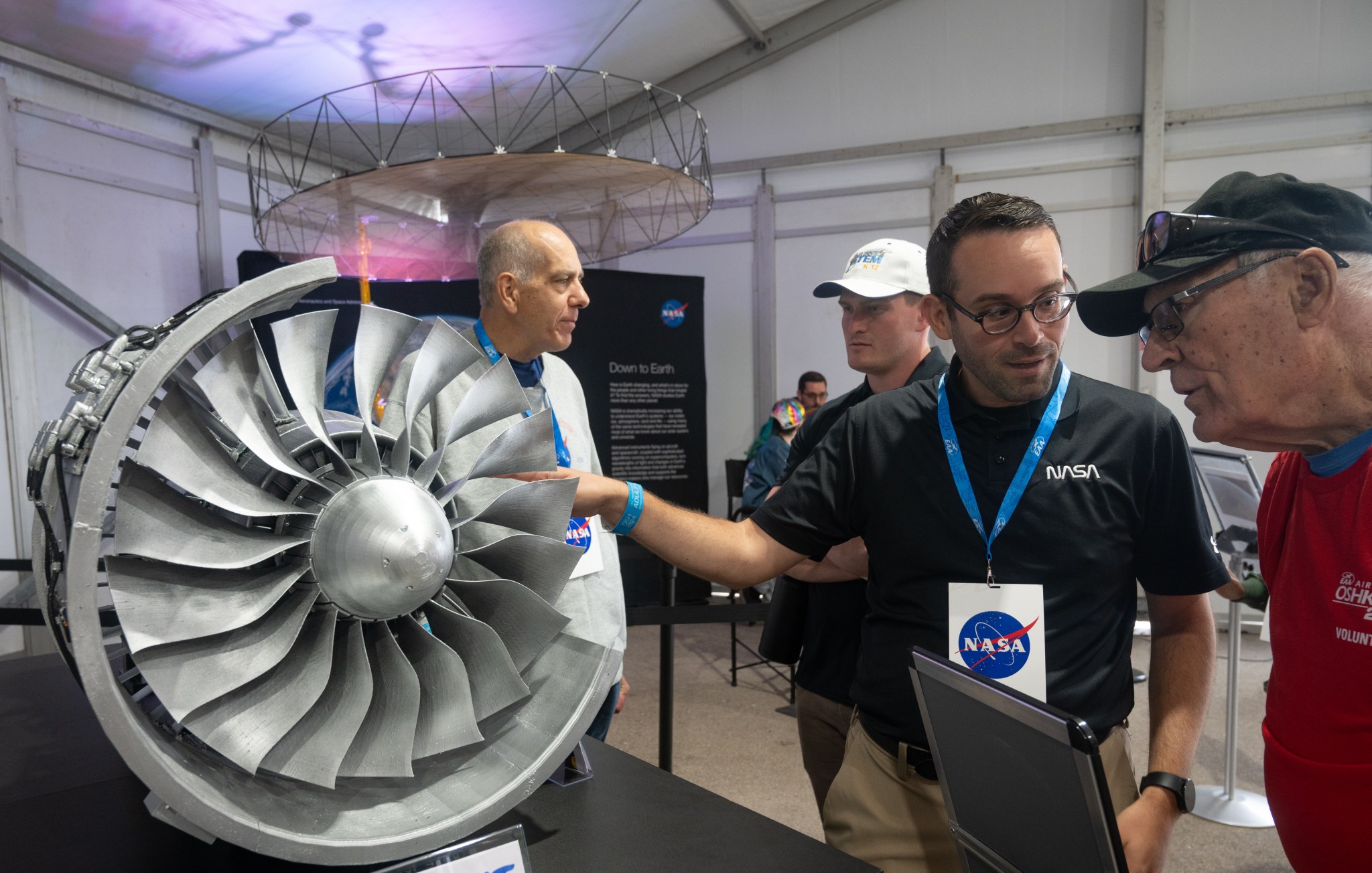 A Glenn specialist places their hand on a turbofan model while providing information to a visitor at EAA AirVenture.