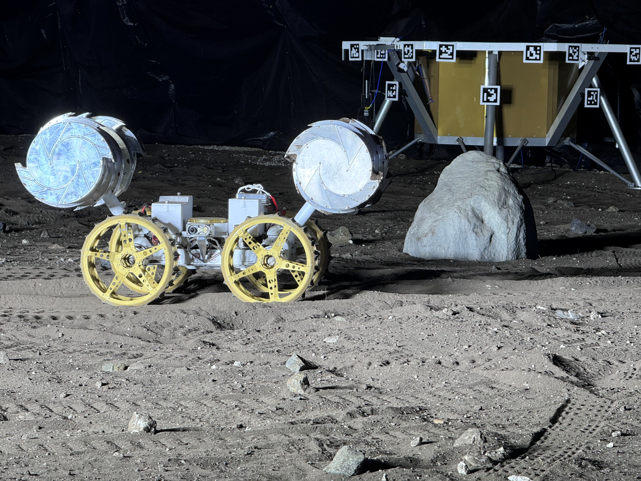 A photo taken from the ISRU Pilot Excavator as it is tested in a blacked out facility with minimal lighting that mimics the harsh, feature-less terrain of the Moon.