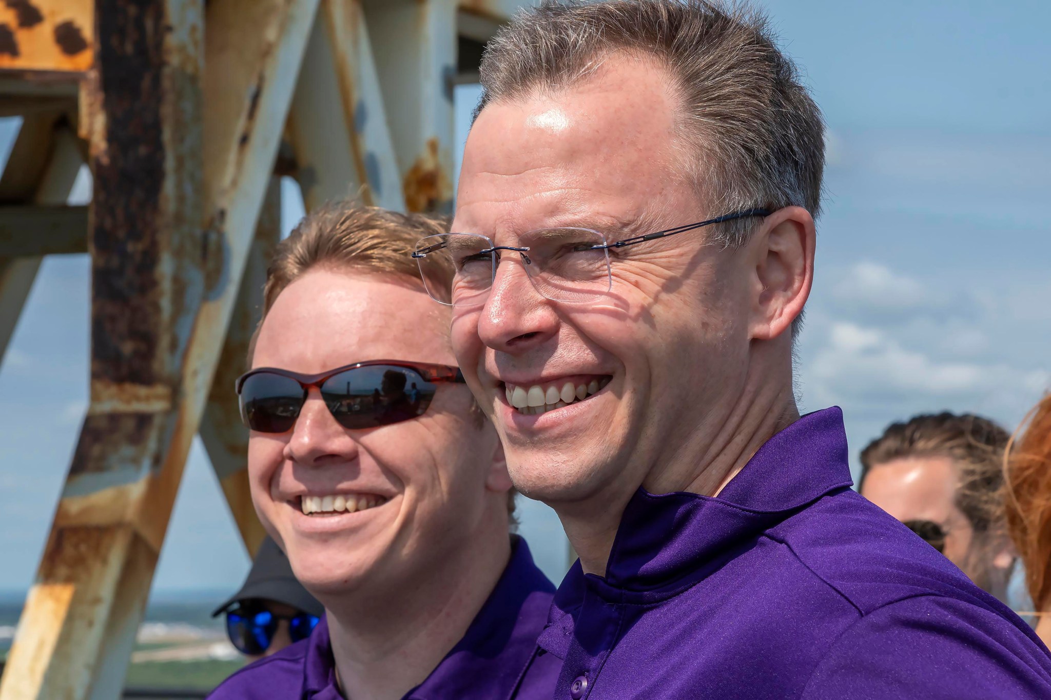 A NASA astronaut and a Roscosmos cosmonaut stand near a launchpad at Kennedy Space Center.