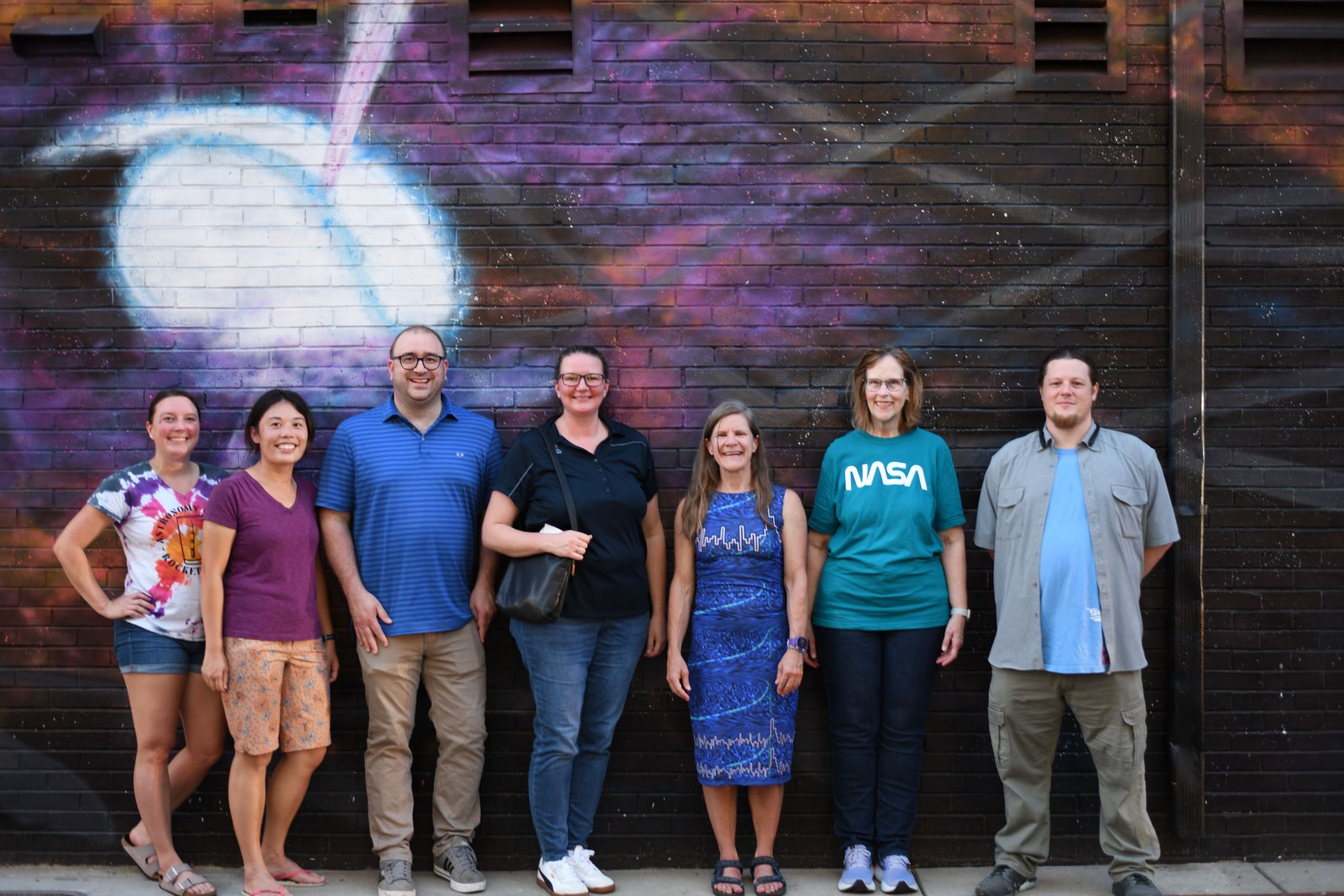 From left to right, scientists and astrophysicists from Marshall, Cori Fletcher, Michelle Hui, Steven Ehlert, Weber, Colleen Wilson-Hodge, Lisa Gibby, and the artist Float pose for a photo in front of the “No Straight Lines” mural at the corner of Clinton Avenue and Washington Street in Huntsville.