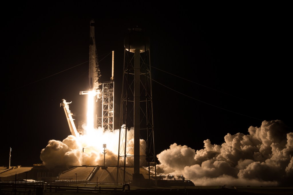 Image shows a SpaceX Falcon 9 rocket lifting off from Launch Complex 39A. A Dragon spacecraft is carrying NASA astronauts Matthew Dominick, Michael Barratt, and Jeanette Epps, and Roscosmos cosmonaut Alexander Grebenkin to the International Space Station.