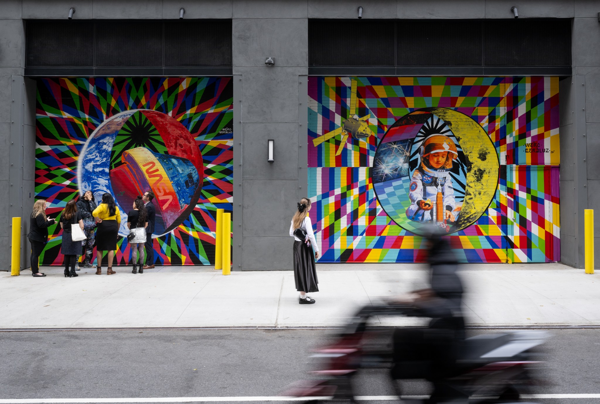 An image of two murals painted on loading dock garage doors. The murals include bold, bright colors and geometric shapes. The image to the left features Earth with a satellite that features the NASA logo. The mural on the right has an image of a child in an astronaut suit playing with toys.