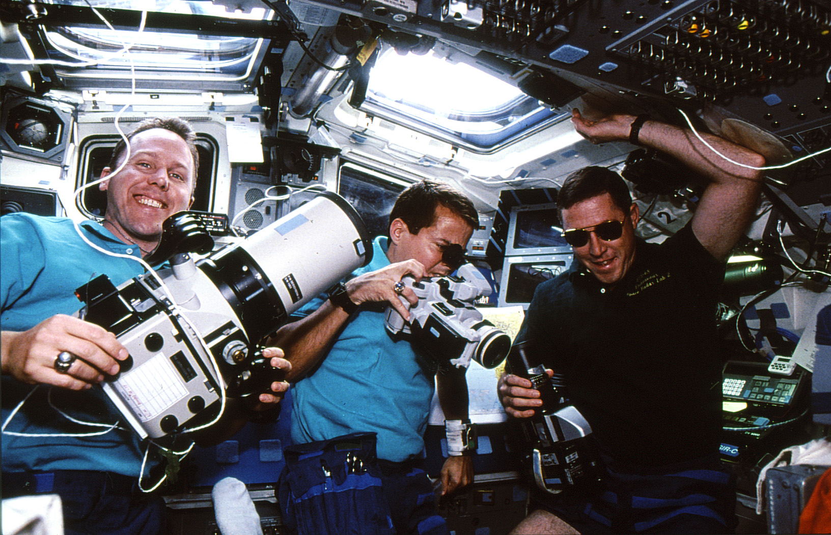 Thomas D. Jones, left, Daniel W. Bursch, and Baker hold various cameras in Endeavour's flight deck