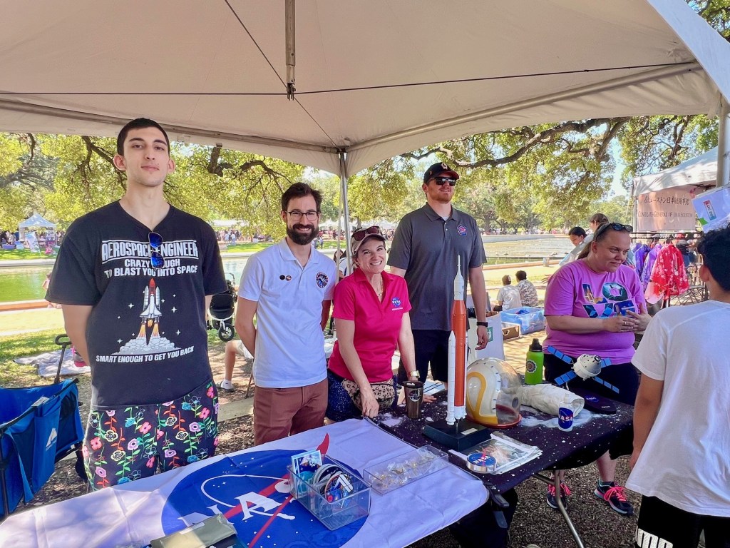 A group of five people stand behind a NASA booth table at an outdoor event.