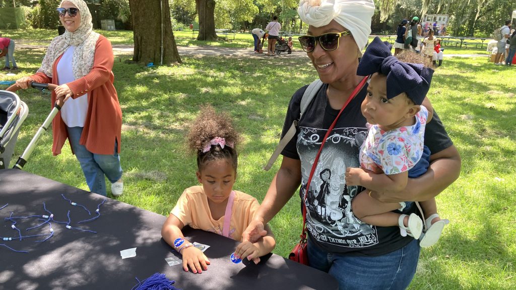 A woman and two small children participate in a bracelet-making activity while attending NASA Day at the Audubon Zoo in New Orleans.