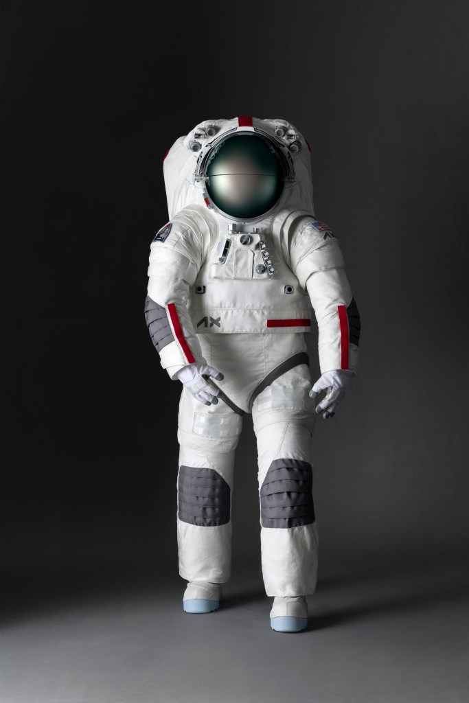 A mockup of the Axiom Space lunar spacesuit design. The majority of the spacesuit is white with grey patches over the knees and elbows and red trimming on the sleeves and torso.