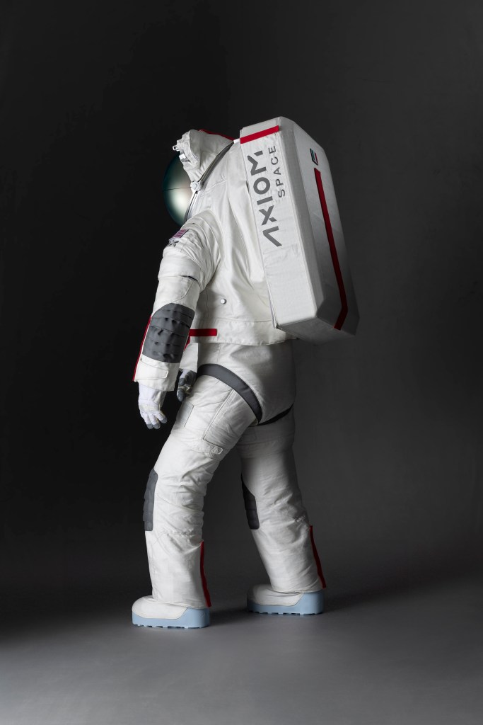 A side view mockup of the Axiom Space lunar spacesuit design. The majority of the spacesuit is white with grey patches over the knees and elbows. There is red trimming on the backpack of the spacesuit with the words Axiom Space shown on the side.