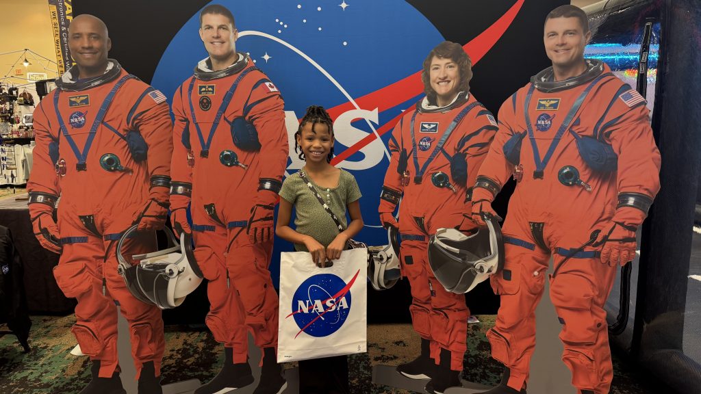 A young participant poses for a photo with life size cardboard cutouts of the Artemis II crew.